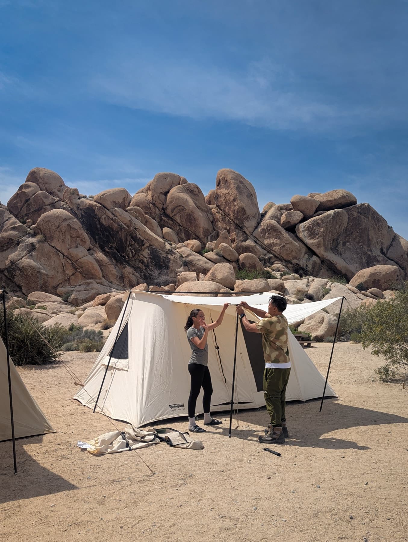 Two people raising a canvas wall tent together among the desert boulders
