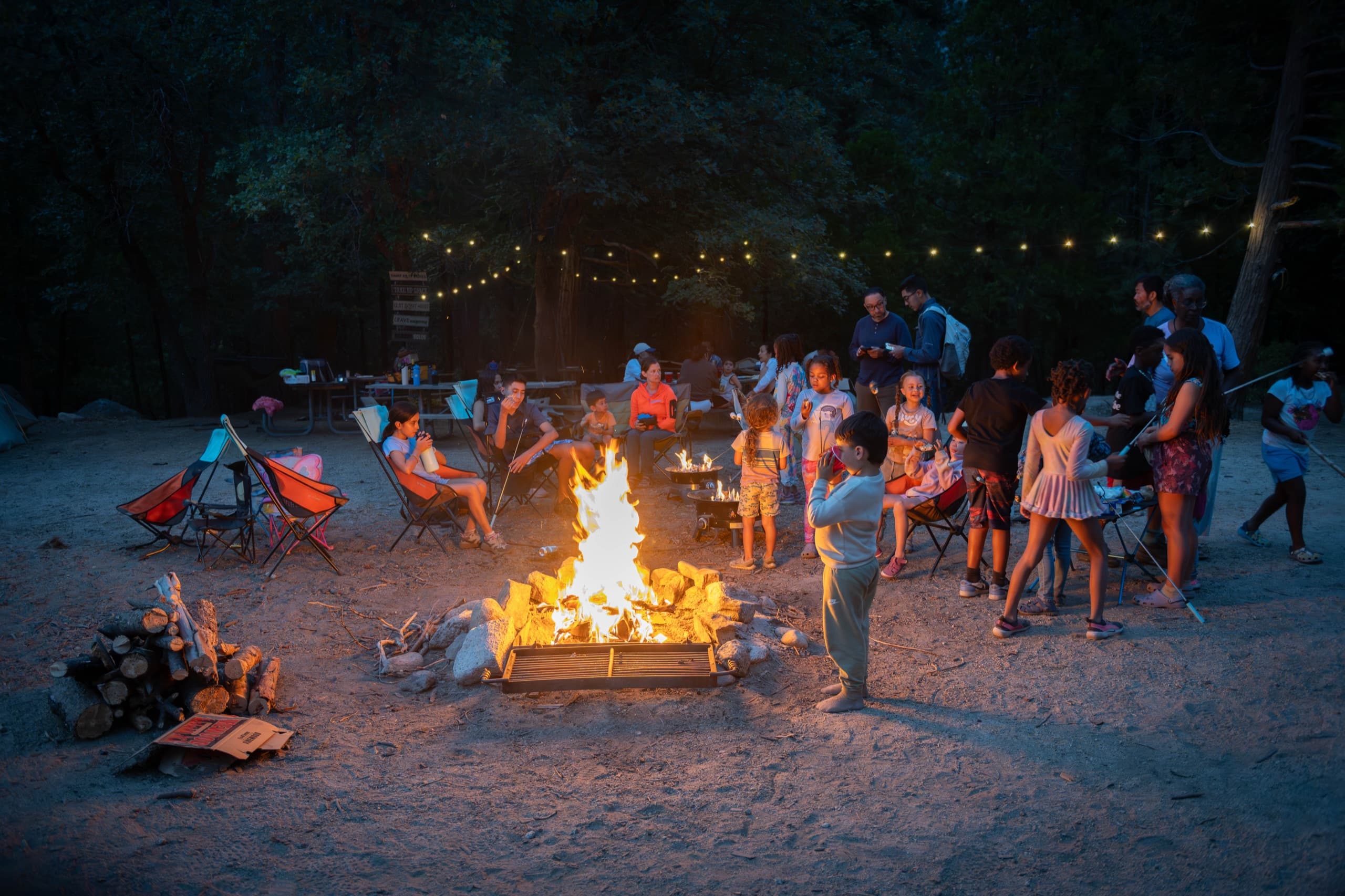 Outdoorithm Collective families gathered around a campfire under string lights at dusk in Kings Canyon