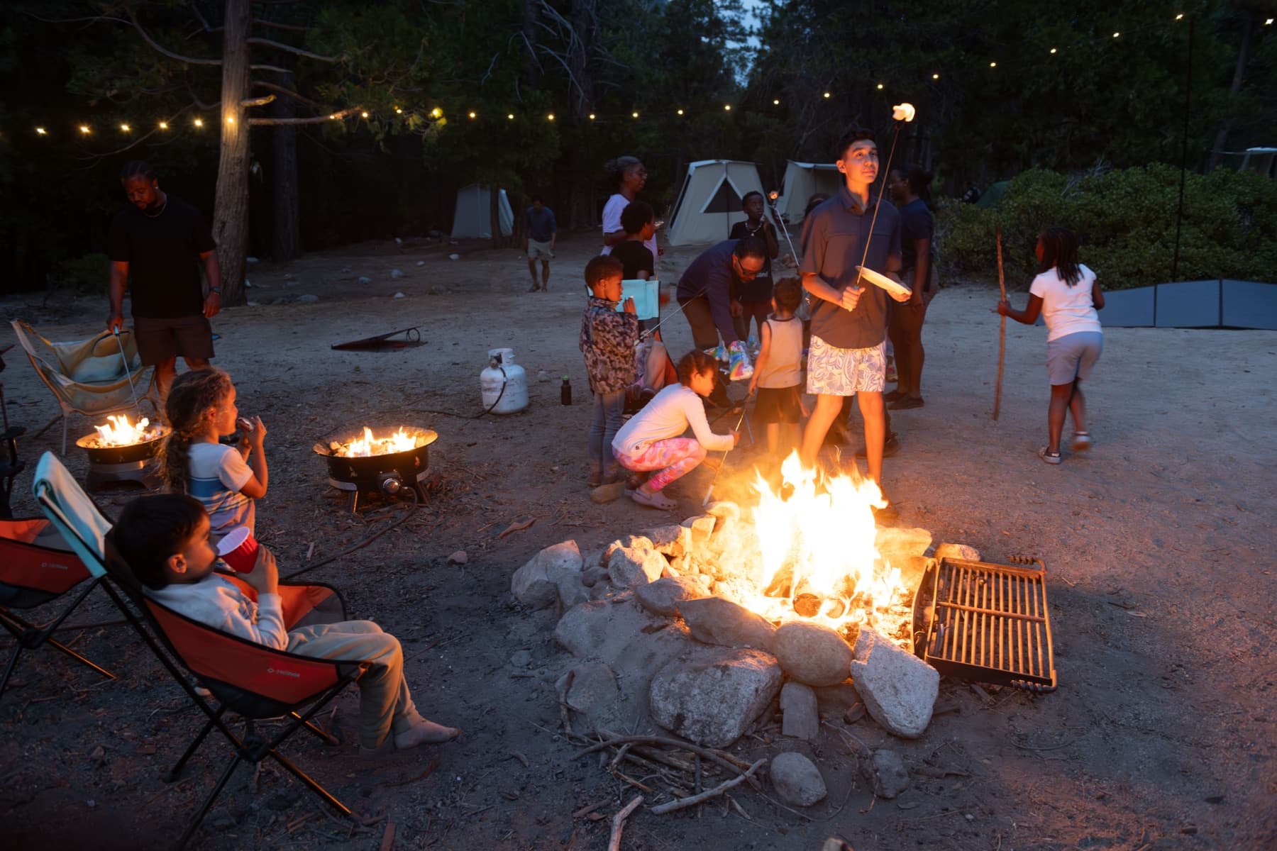 A teenager holds up a toasted marshmallow on a skewer beside the campfire