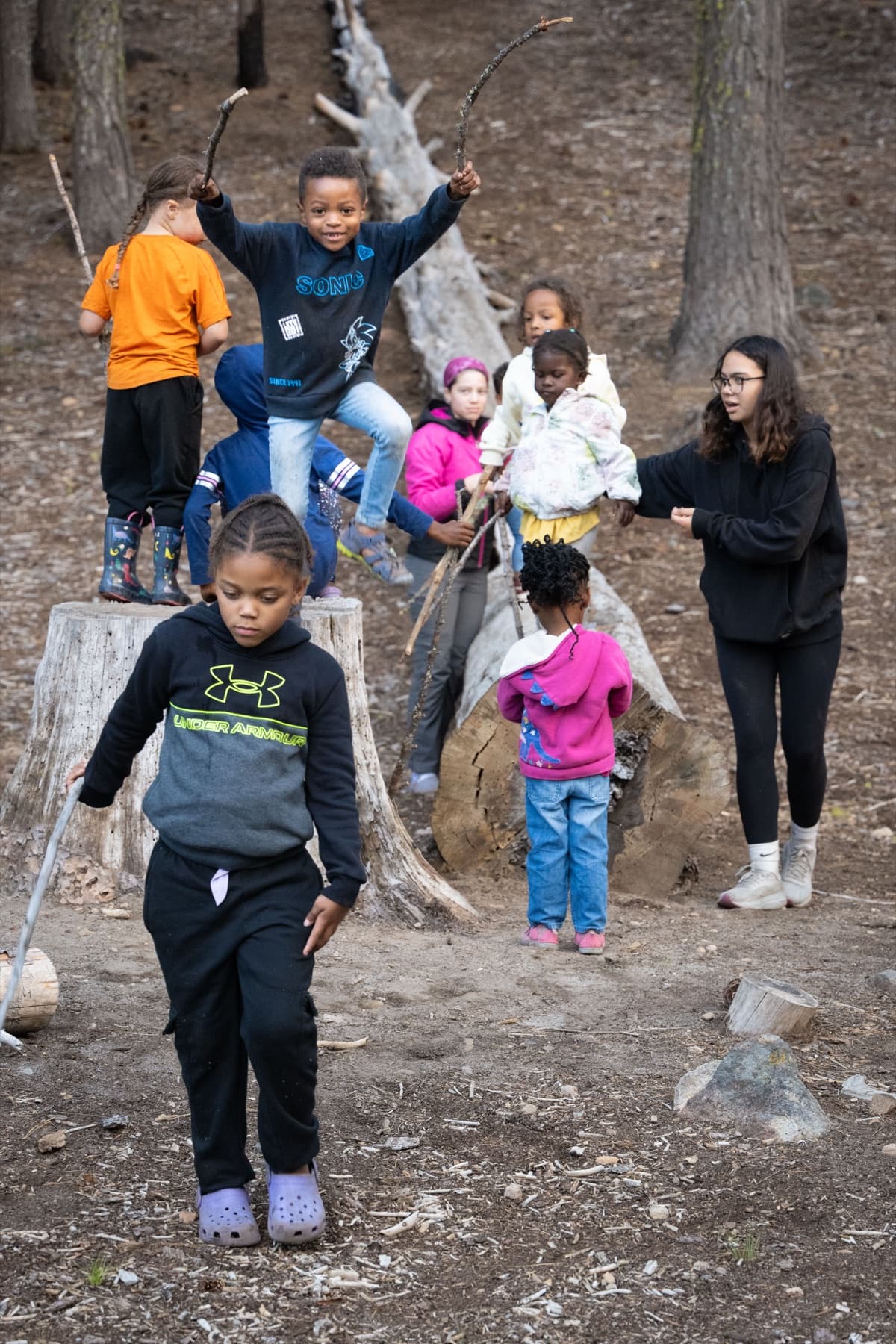 Children playing freely among the trees at camp, two balanced on tree stumps