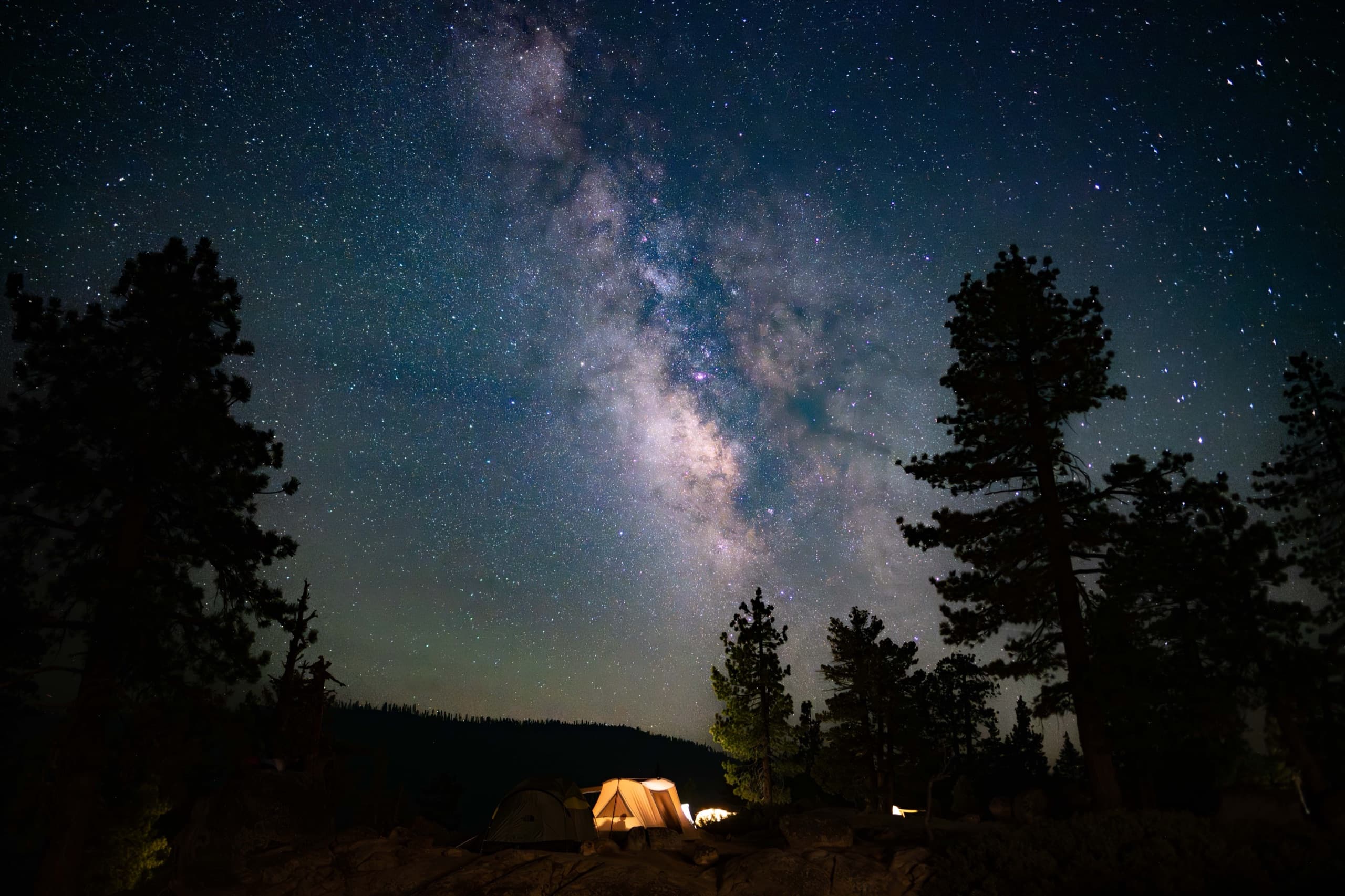 The Milky Way arching over a glowing canvas tent at the Spicer Reservoir camp