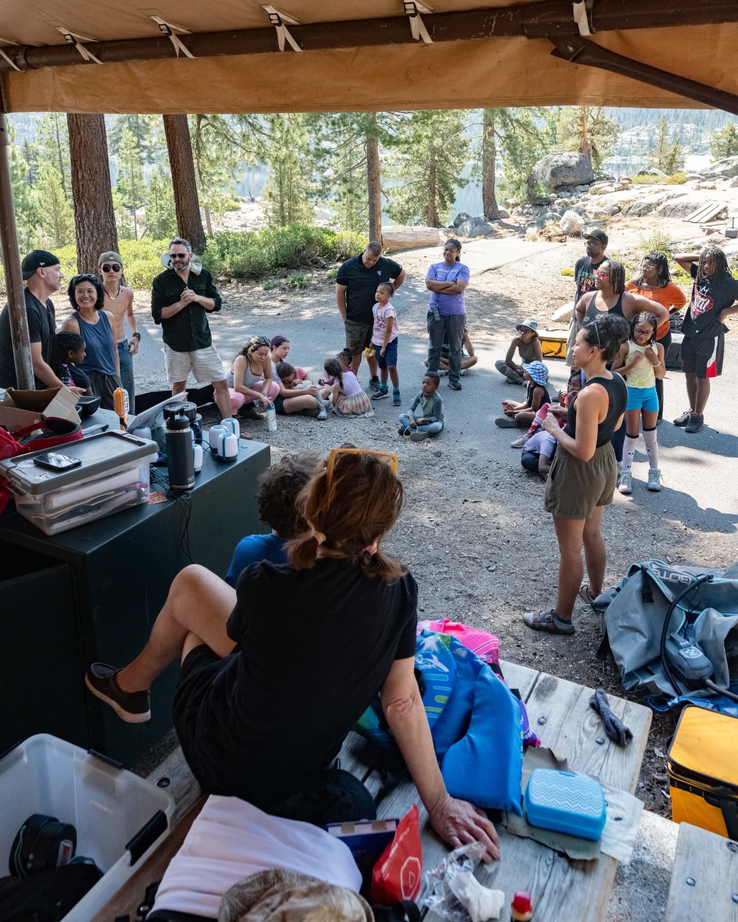 Outdoorithm families gathered in a circle under the camp kitchen canopy for a morning meeting
