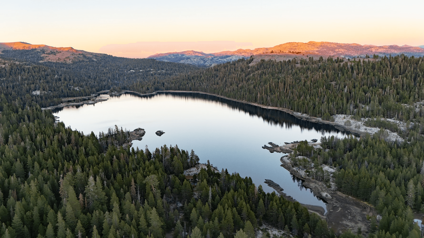 Aerial view of Lake Alpine at golden hour, surrounded by pine forests and mountains